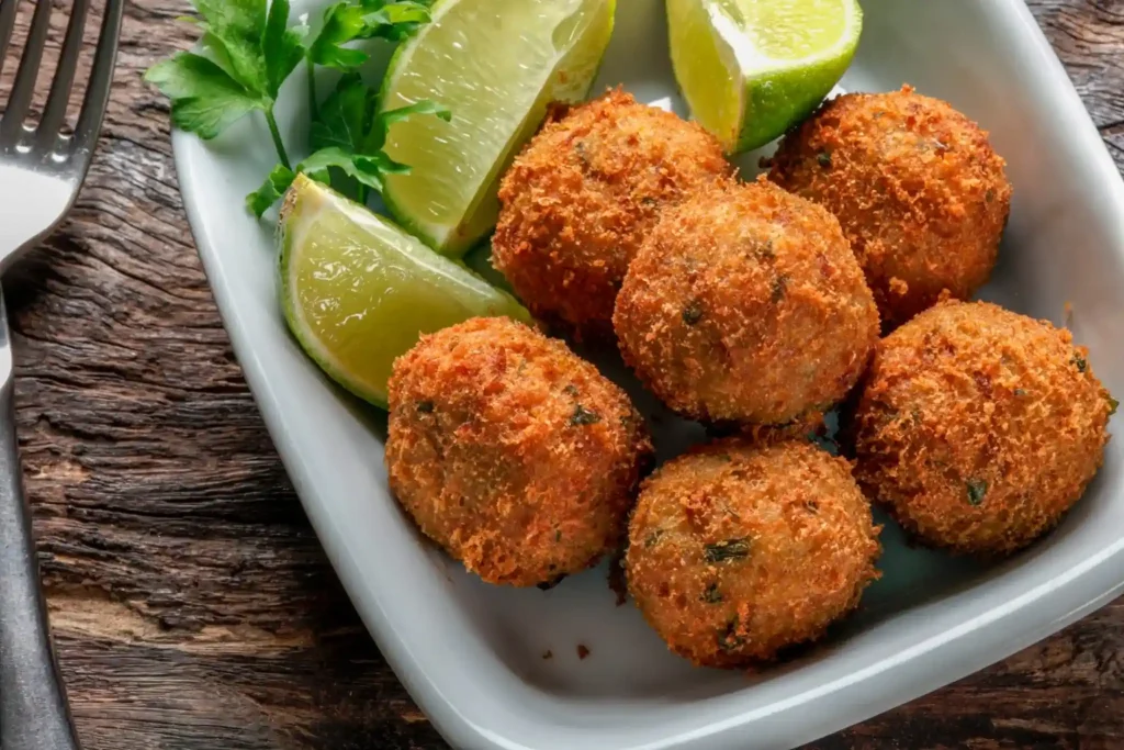 Como fazer bolinho de bacalhau? Bolinhos dourados de bacalhau com limão servidos em prato branco