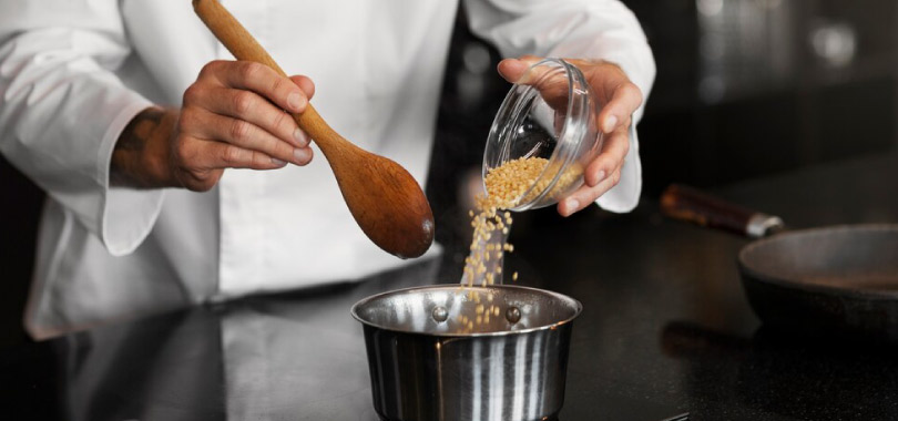 Dia do Profissional da Culinária: conheça mais sobre a data! 2 Mãos de um profissional de cozinha colocando alho num pote.