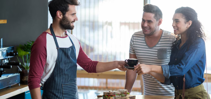 Funcionário entregando xícara de café a um casal.