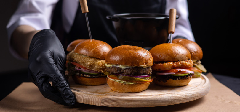 Dicas de combos para hamburgueria 2 Três hambúrgueres sendo levados numa tabua de madeira.