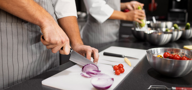 Confira dicas de como melhorar a produtividade na cozinha 2 Chef de cozinha fatiando cebola roxa.
