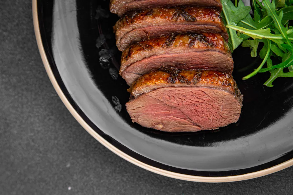 Carne ao ponto Carne ao ponto fatiada em prato preto, com interior rosado e crosta dourada, pronta para servir