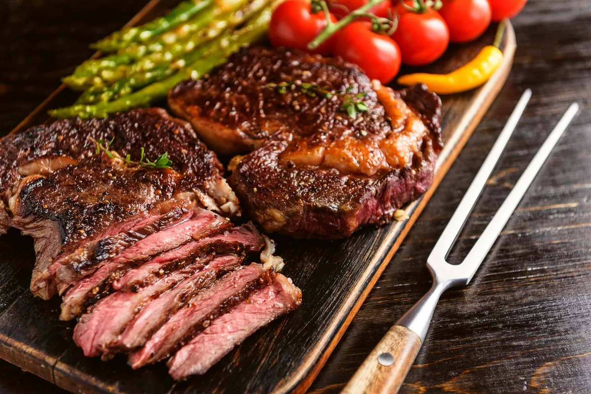 Cortes bovinos: guia com tabela, mapa e dicas de preparo 2 Melhores cortes bovinos para churrasco grelhados sobre tábua de madeira com tomate e aspargos
