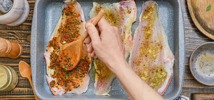 Como temperar peixe: técnicas e temperos para valorizar os preparos 1 Pessoa temperando filé de peixe.